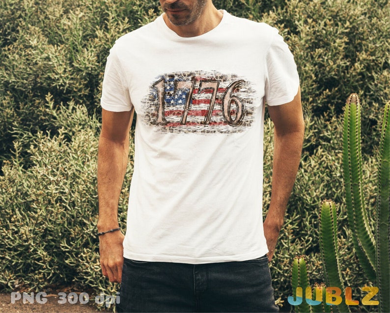 May include: White t-shirt with a distressed American flag design and the text "1776" printed on the front.