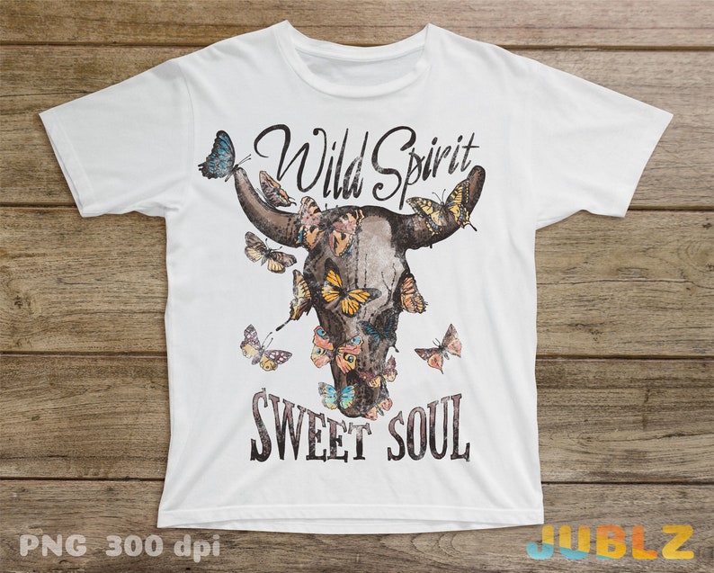 May include: White t-shirt with a brown bull skull design with colorful butterflies and the text "Wild Spirit Sweet Soul".