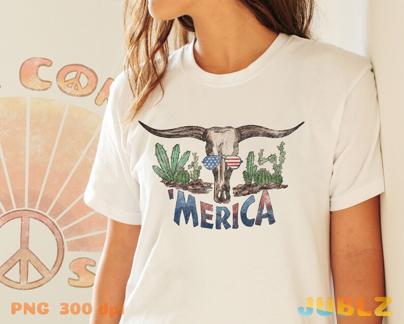 May include: White t-shirt with a distressed graphic of a cow skull wearing sunglasses and surrounded by cacti. The text 'MERICA' is printed below the skull.