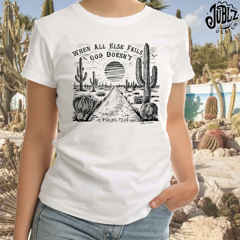 May include: A white t-shirt with a black and white illustration of a desert landscape with cacti and a road. The text "When all else fails God doesn't" is above the illustration. The text "Psalms 73:26" is below the illustration.