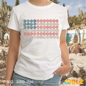 May include: White t-shirt with a graphic of a stylized American flag made of daisies. The daisies are red, white, and blue.
