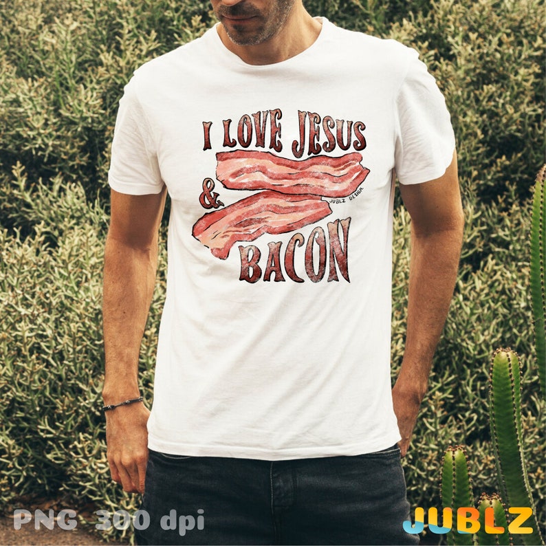 Puede incluir: Una camiseta blanca con el texto "I love Jesus & Bacon" impreso en ella. El texto est&aacute; en un esquema de colores rojo, blanco y azul. La imagen del tocino est&aacute; en un estilo acuarela.
