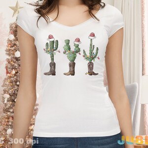 K&ouml;nnte beinhalten: Wei&szlig;es T-Shirt mit einem Weihnachtskaktus, der einen Weihnachtsmann-Hut und Stiefel tr&auml;gt. Der Kaktus ist mit bunten Lichtern geschm&uuml;ckt.