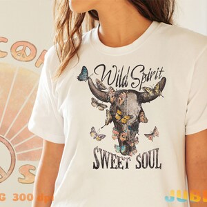 May include: White t-shirt with a graphic of a cow skull with butterflies and the text "Wild Spirit Sweet Soul".