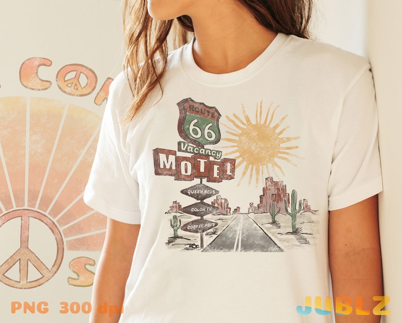 May include: White t-shirt with a vintage Route 66 Motel graphic. The graphic features a retro sign with the text "Route 66 Vacancy Motel" and a sun with rays. The graphic also includes a desert landscape with cacti and a road.