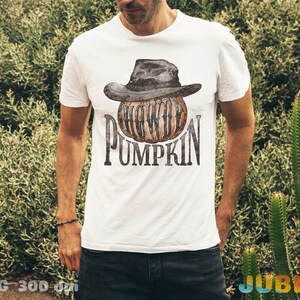 May include: A white t-shirt with a graphic of a pumpkin wearing a black cowboy hat. The text "Howdy Pumpkin" is printed on the shirt.