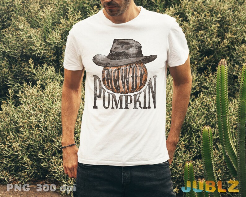 May include: A white t-shirt with a graphic of a pumpkin wearing a black cowboy hat. The text "Howdy Pumpkin" is printed on the shirt.