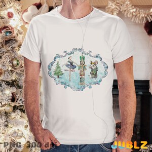 May include: A white t-shirt with a vintage-style illustration of a ballerina, a nutcracker, and a mouse in a blue and white frame. The illustration is surrounded by a decorative border.