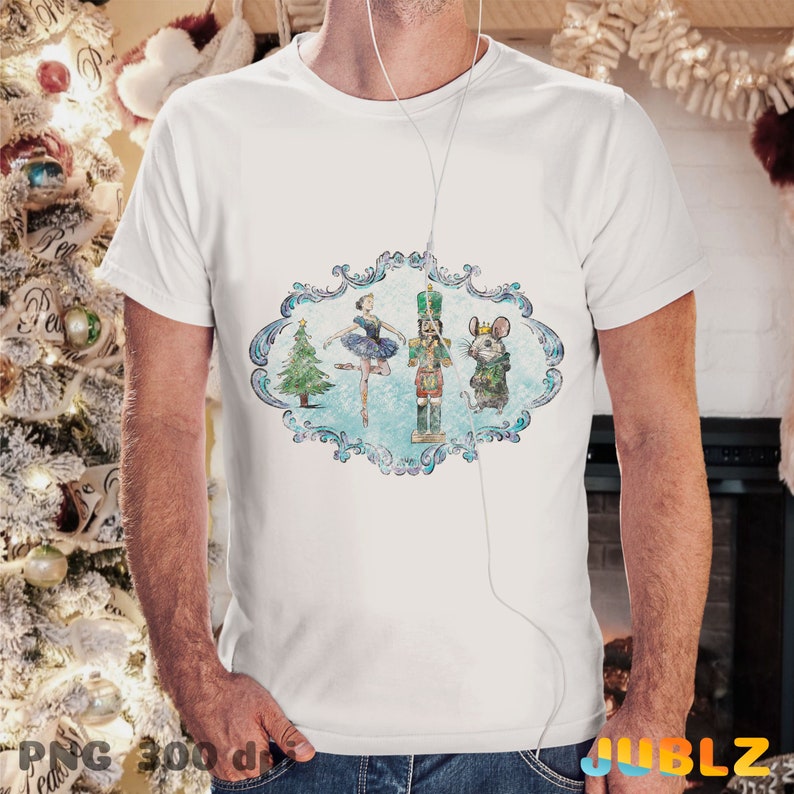 May include: A white t-shirt with a vintage-style illustration of a ballerina, a nutcracker, and a mouse in a blue and white frame. The illustration is surrounded by a decorative border.
