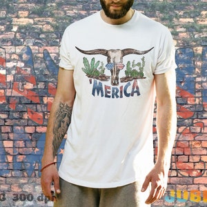 May include: White t-shirt with a skull wearing sunglasses and a red, white, and blue bandana. The skull is surrounded by cacti and the text 'MERICA' is below the skull.