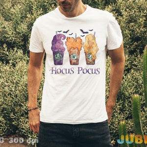 May include: White t-shirt featuring a design of three Halloween-themed coffee cups with the text "Hocus Pocus" underneath.