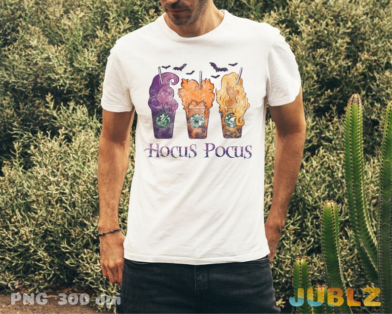 May include: White t-shirt featuring a design of three Halloween-themed coffee cups with the text "Hocus Pocus" underneath.