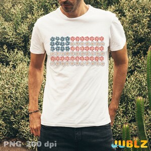 May include: White t-shirt with a red, white, and blue American flag design made of flowers. The flag is centered on the shirt.