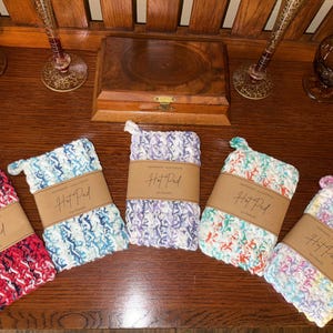 May include: Five crocheted hot pads in different colors and patterns. Each pad has a brown tag with the text "Hot Pad" printed on it.