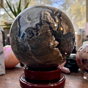 May include: A large, dark gray and brown agate sphere on a wooden stand. The sphere has a swirling pattern of black, brown, and white.