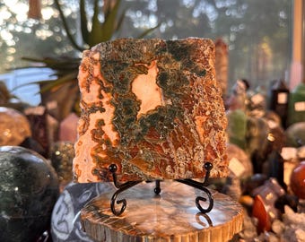 May include: A large, square, green, orange, and white agate slab on a wooden stand. The agate has a unique pattern of swirling colors and textures.