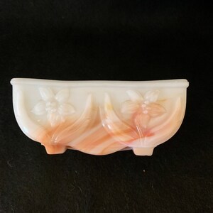 May include: A white and orange swirl glass dish with a scalloped edge and floral design. The dish has three small feet.