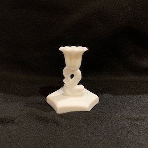May include: White ceramic candle holder with a flower-shaped top and a base shaped like a stylised figure.
