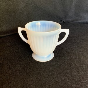 May include: A white, opaque, ribbed, two-handled sugar bowl with a blue tint on the inside.