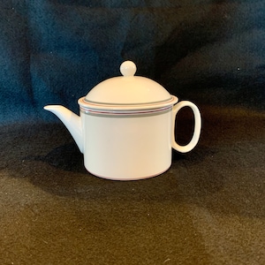 May include: White teapot with a lid, featuring a red and gray striped band around the body. The teapot has a round handle and a spout.