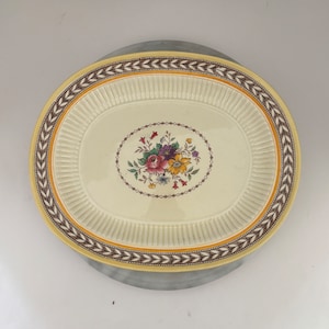 May include: A white oval serving dish with a brown and gold floral border. The center of the dish features a floral design with pink, yellow, and purple flowers.