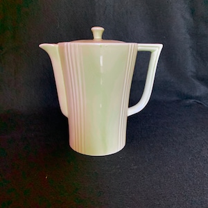 May include: A pale green ceramic coffee pot with a lid and a handle. The pot has vertical lines on the body.