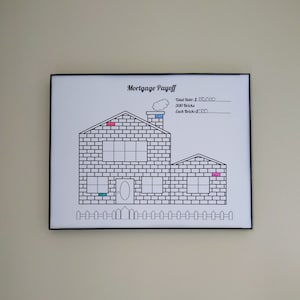 May include: A black framed chart with a white background showing a house made of bricks. The house is divided into 300 bricks, each representing $500. The chart is titled "Mortgage Payoff" and includes the text "Total Debt: $50,000. 300 Bricks Each Brick $500".