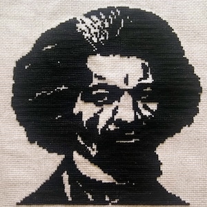 May include: Black and white cross-stitch portrait of a man with a large afro hairstyle. The man is wearing a dark suit.