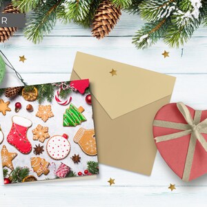 May include: A Christmas card with a festive design featuring gingerbread cookies, candy canes, and a Christmas tree. The card is on a white wooden surface with a brown envelope and a heart-shaped gift box.