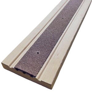 Peut inclure: Un seuil de porte en bois avec un insert antidérapant texturé marron. Le bois clair présente un motif rainuré de chaque côté de l'insert. Deux petits trous sont percés dans l'insert. Ce produit est conçu pour la sécurité.