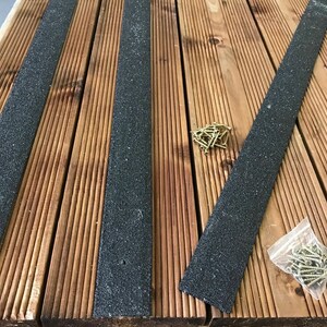 Könnte beinhalten: Vier schwarze Anti-Rutsch-Streifen für Terrassenböden im Freien, mit einem Haufen goldener Schrauben und einer Tüte Schrauben im Hintergrund.