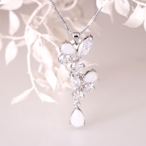 May include: A silver necklace with a pendant featuring a cluster of white pear-shaped and round stones. The pendant is designed in a cascading, floral-like pattern.