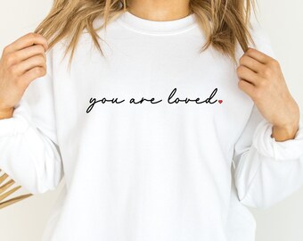 Op de afbeelding: Witte trui met de tekst "you are loved." in zwarte letters met een klein rood hartje.