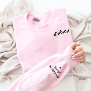 May include: Pink sweatshirt with the Tamil words "amma" and "love you" on the front and sleeve, respectively.
