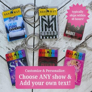May include: A collection of rectangular keychains featuring various Broadway musical playbill designs, including Dear Evan Hansen, Beetlejuice, Hadestown, Six, Moulin Rouge, and Mean Girls, each attached to a silver metal split ring and chain.