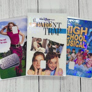 Może przedstawiać: Trzy okładki filmów na DVD: "Stowarzyszenie Umarłych Poetów", "Rodzice, miejcie się na baczności" i "High School Musical 2". Okładka "Stowarzyszenie Umarłych Poetów" przedstawia kobietę w różowym stroju. "Rodzice, miejcie się na baczności" ma zdjęcia dwóch dziewczyn. "High School Musical 2" ma grupę ludzi.