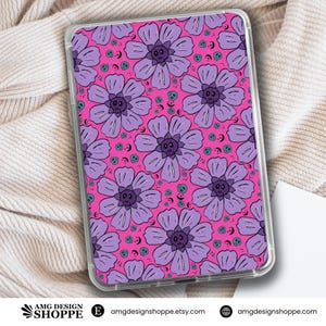 Könnte beinhalten: Eine transparente Handy- oder Tablet-Hülle mit einem sich wiederholenden Muster aus lila Blumen mit Totenkopf-Zentren auf einem leuchtend pinkfarbenen Hintergrund. Kleine türkisfarbene Totenköpfe und Halbmonde füllen die Zwischenräume.