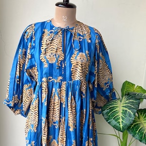 May include: A blue dress with vertical stripes and a repeating tiger pattern. The dress has long sleeves and a tie at the neckline. The dress is displayed on a mannequin.