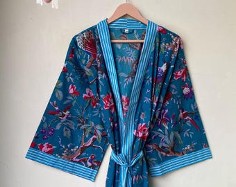 May include: A teal-colored robe with a floral and bird pattern, hanging on a wooden hanger. The robe has a striped trim and a matching belt. The floral pattern includes red and purple flowers.