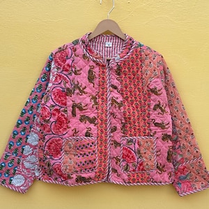 May include: Pink quilted jacket with floral and animal embroidery. The jacket has a round collar, two pockets, and a zipper closure. The sleeves are a different pattern than the body of the jacket. The jacket is hanging on a wooden hanger.