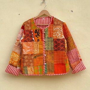 以下が含まれることがあります： ボタン留めのパッチワークキルトジャケット。ジャケットはオレンジ、ブラウン、グリーンの色合いのさまざまな生地で作られています。生地には、ストライプ、チェック、花柄など、さまざまなパターンがあります。ジャケットは袖口と裾に赤と白のストライプのトリムが付いています。