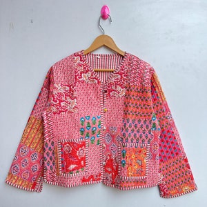 Puede incluir: Una chaqueta acolchada rosa con un diseño de patchwork que presenta varios patrones florales y geométricos. La chaqueta tiene un cierre de botón y mangas largas.