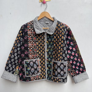 Puede incluir: Una chaqueta acolchada negra con un diseño de patchwork que presenta varios patrones florales y geométricos. La chaqueta tiene un cuello y puños a rayas blancas y negras.