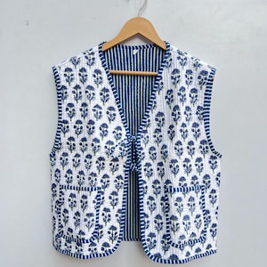 May include: A white quilted vest with a blue floral print and blue and white striped lining. The vest has two pockets and a tie closure.