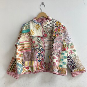 Könnte beinhalten: Eine Patchwork-Steppjacke mit verschiedenen floralen und geometrischen Mustern in Rosa, Blau, Grün, Gelb und Braun. Die Jacke hat einen Stehkragen und einen Knopfverschluss.