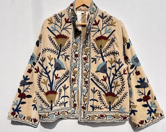 以下が含まれることがあります： 青、赤、金色の花柄が刺繍されたベージュのジャケット。スタンドカラーと長袖です。