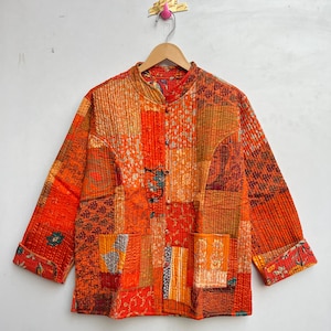 Könnte beinhalten: Eine Patchwork-Jacke in Orange-, Rot- und Brauntönen hängt an einem Holzbügel. Die Jacke hat einen Stehkragen, lange Ärmel und eine Knopfleiste. Der Stoff ist eine Mischung aus gemusterten und unifarbenen Teilen.