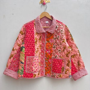 Könnte beinhalten: Eine Patchwork-Jacke in Rosa-, Orange- und Weißtönen mit Kragen und zwei Vordertaschen. Die Jacke hat ein gestepptes Design mit Blumen- und Tigerdruckmustern. Die Manschetten und der Kragen sind mit rot-weißen Streifen versehen.