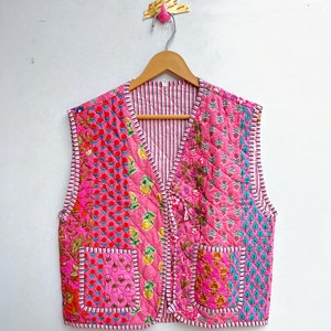 May include: A pink quilted vest with a floral print and two pockets. The vest has a V-neck and is made of cotton.