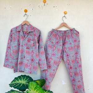 May include: A gray and pink floral pajama set with white piping. The top has a collared neckline and long sleeves. The pants have an elastic waistband.